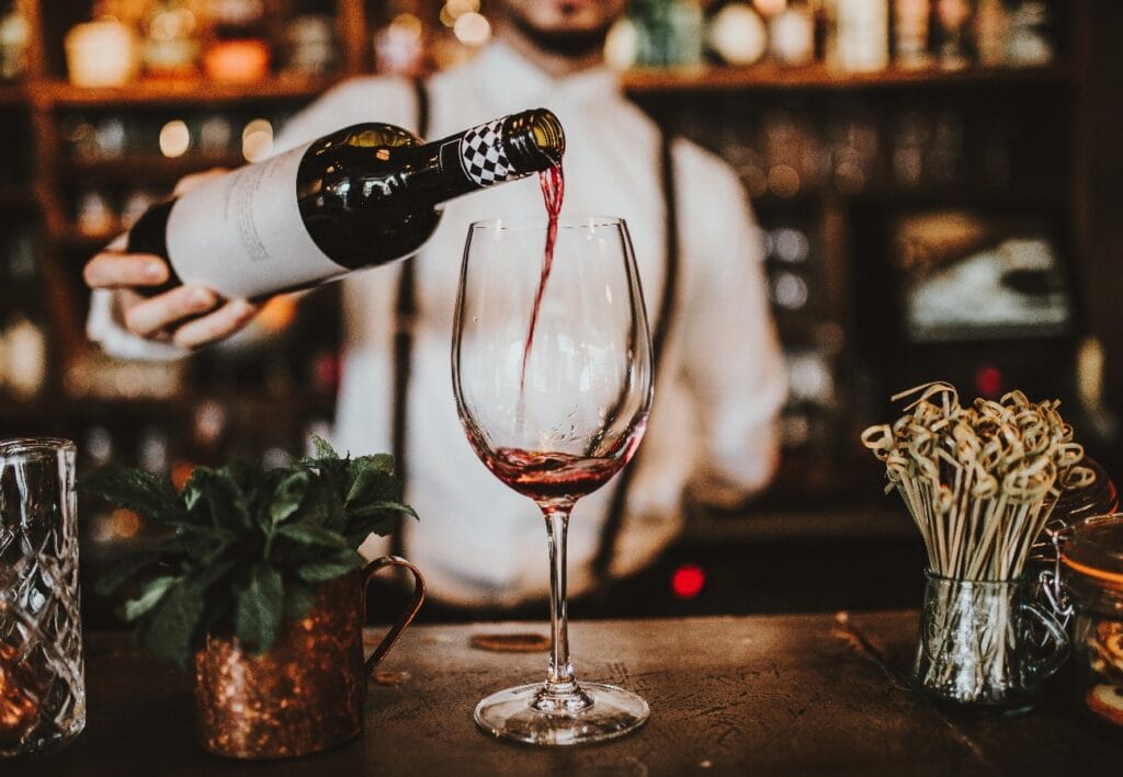 Nahaufnahme eines Barkeepers, der Rotwein in ein Glas gießt. Hosp