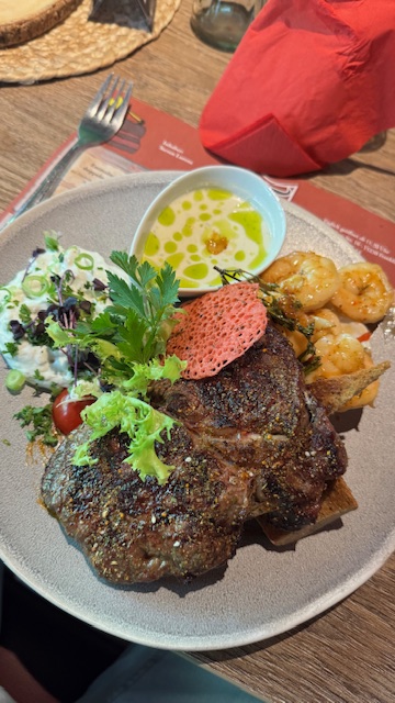Ein medium gebratenes Steak mit cremigem Dip, Garnelen und frischem Gemüsesalat
