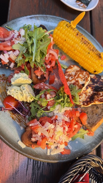 Ein buntes Tellergericht mit gegrilltem Maiskolben, Halloumi, Brot und frischem Salat
