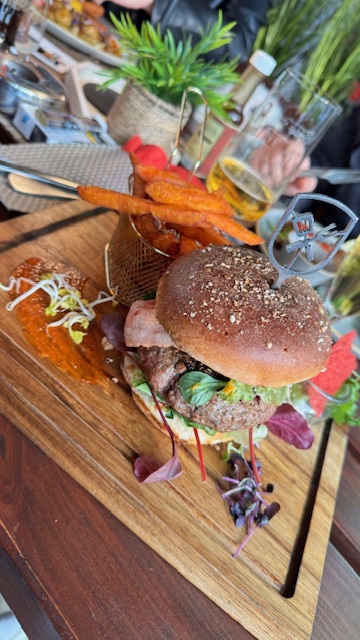 Ein saftiger Burger mit frischem Salat und Süßkartoffelpommes auf Holzbrett