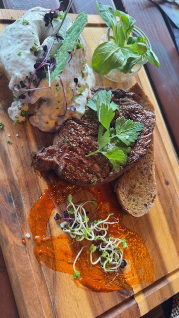 Ein saftiges Steak mit frischen Kräutern auf Holzbrett, Brot und Dips bunt angerichtet