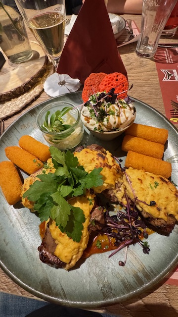 Ein Teller mit überbackenem Fleisch, Kroketten, frischem Salat und bunter Deko