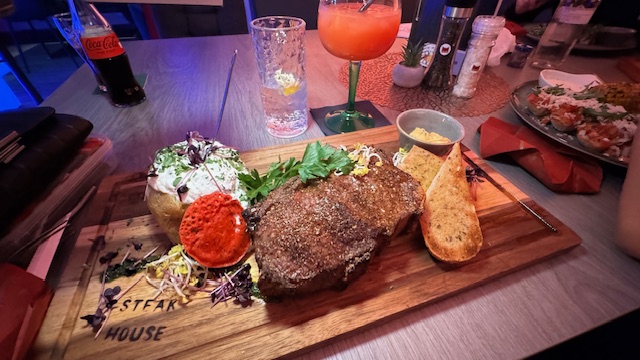 Ein saftiges Steak mit Ofenkartoffel, Kräutern und Toast auf einem Holzbrett serviert