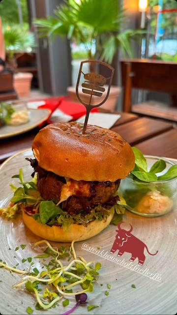 Ein saftiger Burger mit grünem Salat, Sprossen und Sauce auf einem hellen Teller